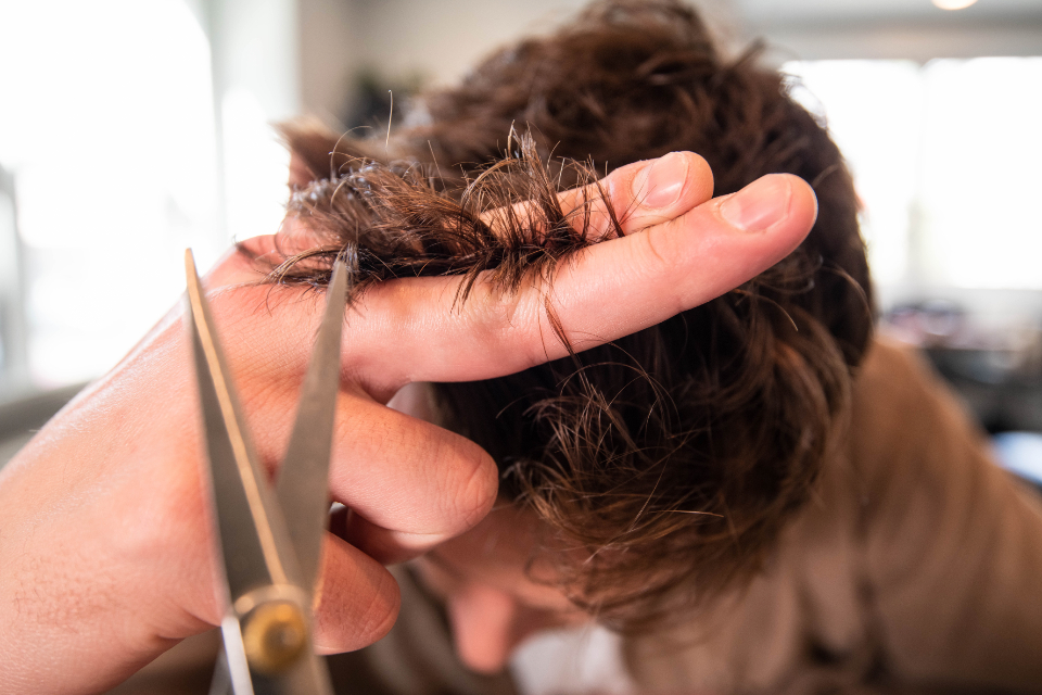 Handen die met schaar en kam een lok haar bijknippen